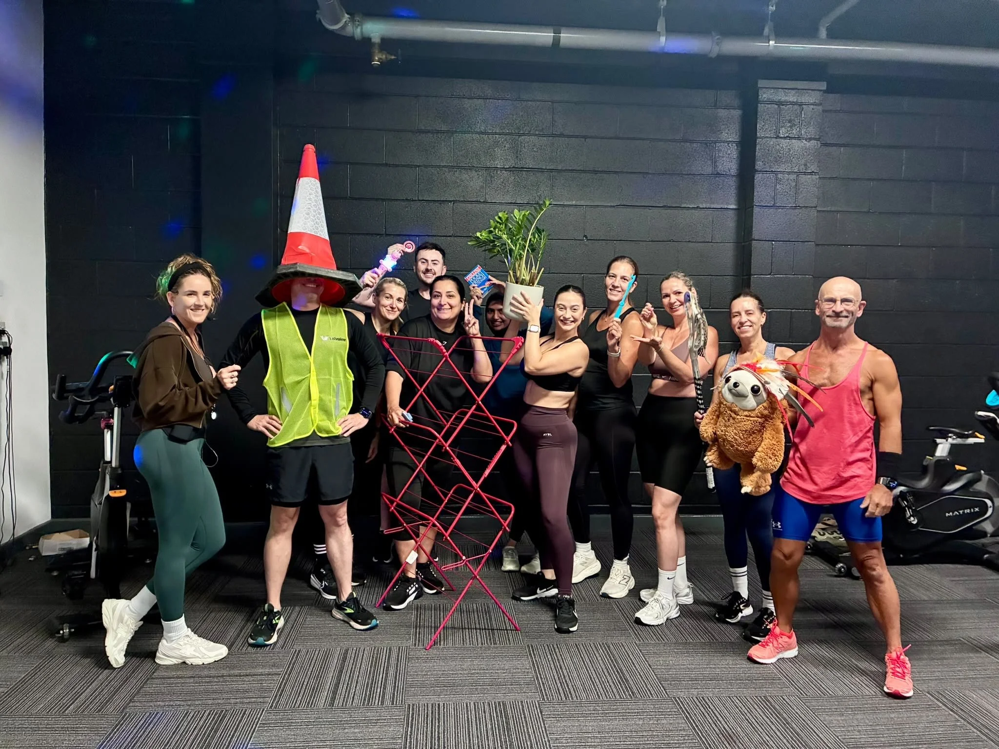 Class members smiling beside the spin bikes, including a traffic-cone outfit