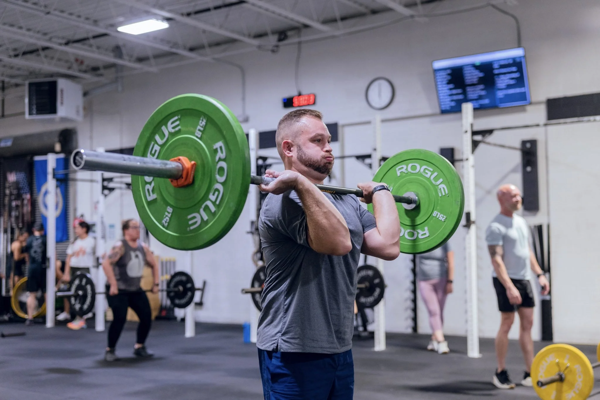 Member front-racking a barbell loaded with green bumper plates during a CrossFit class