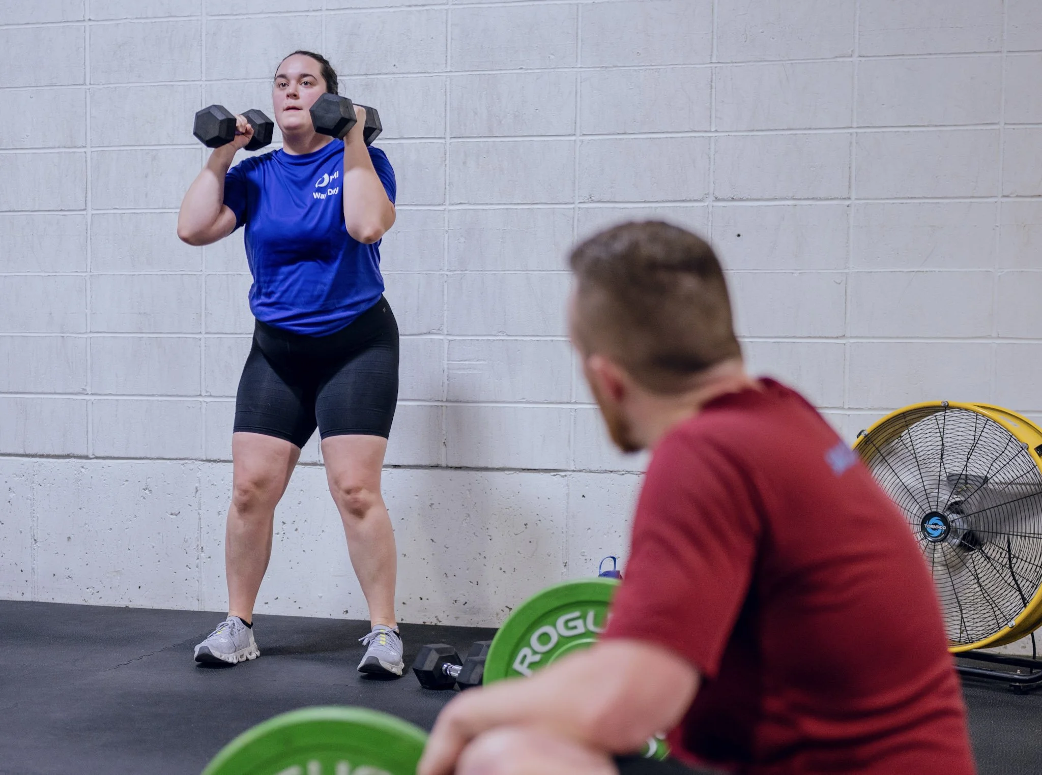 Coach watching a member press dumbbells overhead