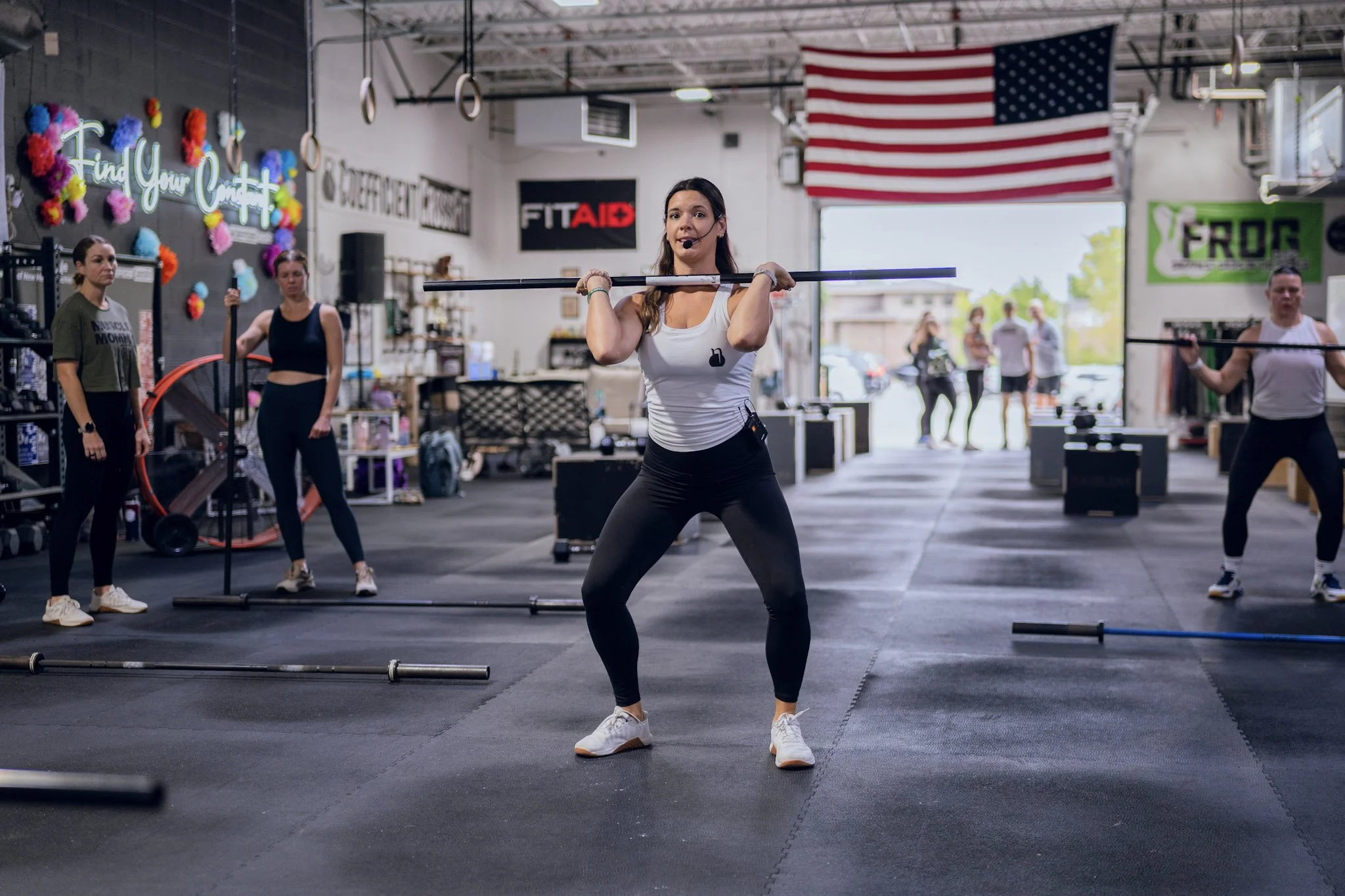 Member front-squatting a barbell during a CrossFit class, with the class training behind her