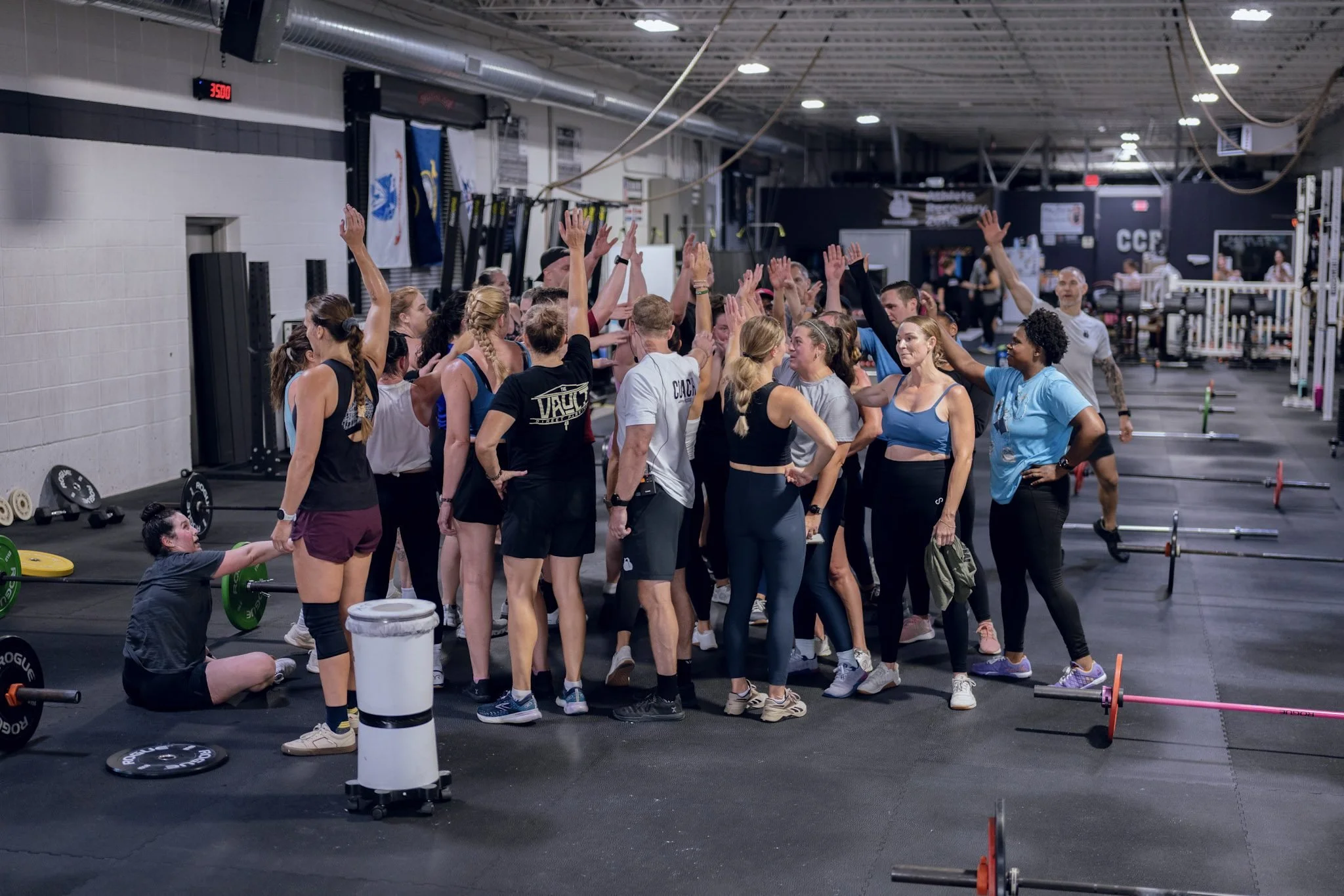 A big group of CCF athletes huddled together with hands raised after a workout