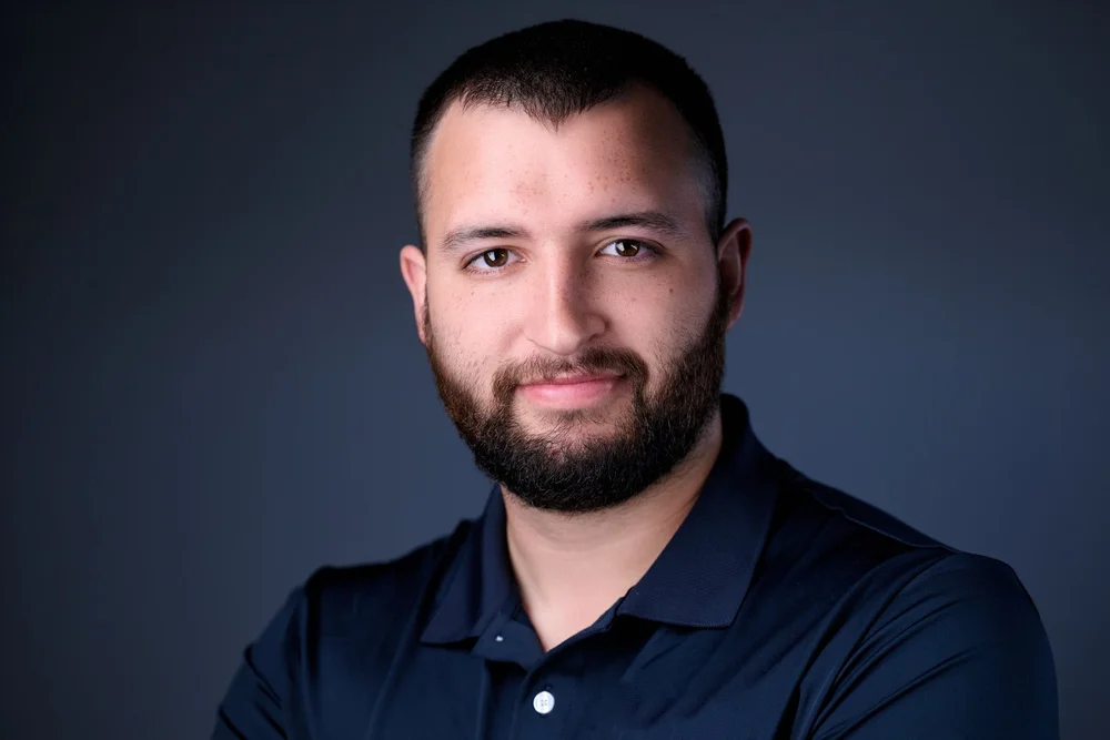 Corporate headshot of a man in a navy shirt, photographed in Syracuse NY