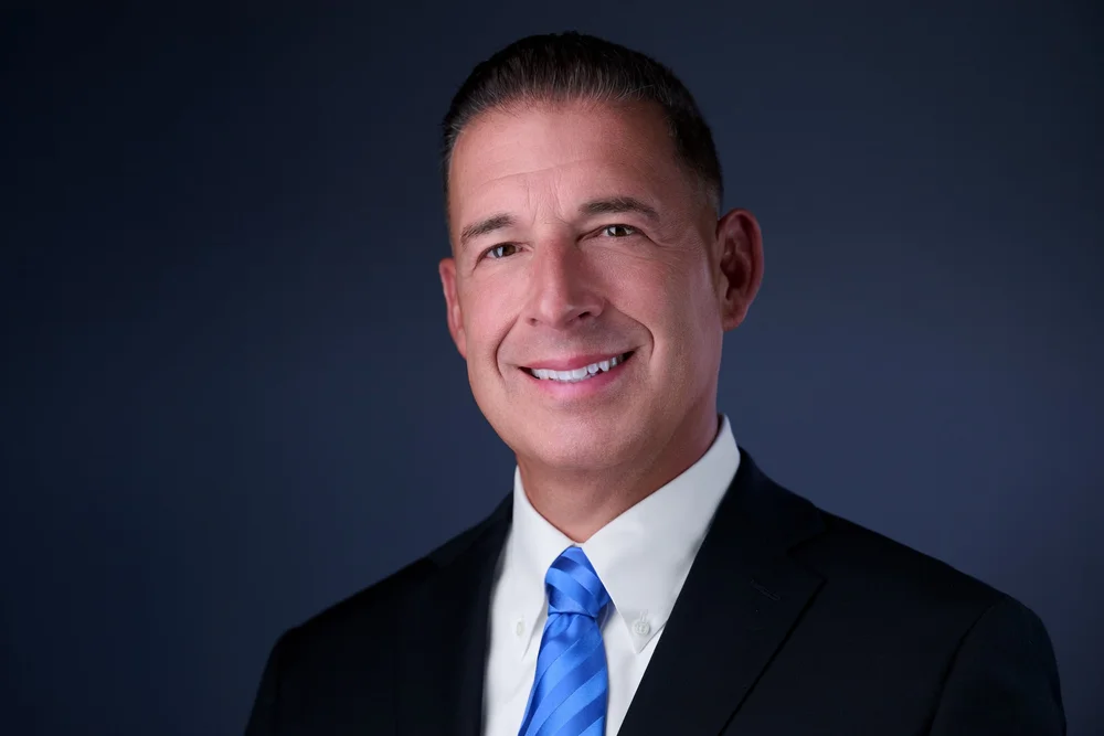 Executive headshot of a man in a dark suit and blue tie, Syracuse NY
