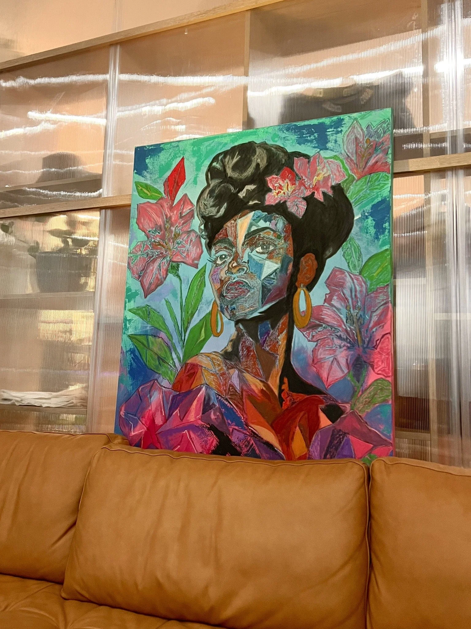 A floral portrait by Wyntress X’ion displayed behind a caramel leather sofa.