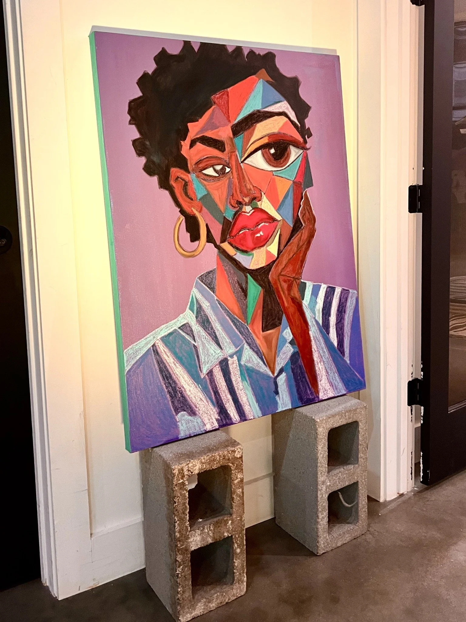 A colorful geometric portrait against a purple background, displayed on concrete blocks.