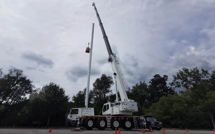 Crane lifting a work basket up a stealth monopole