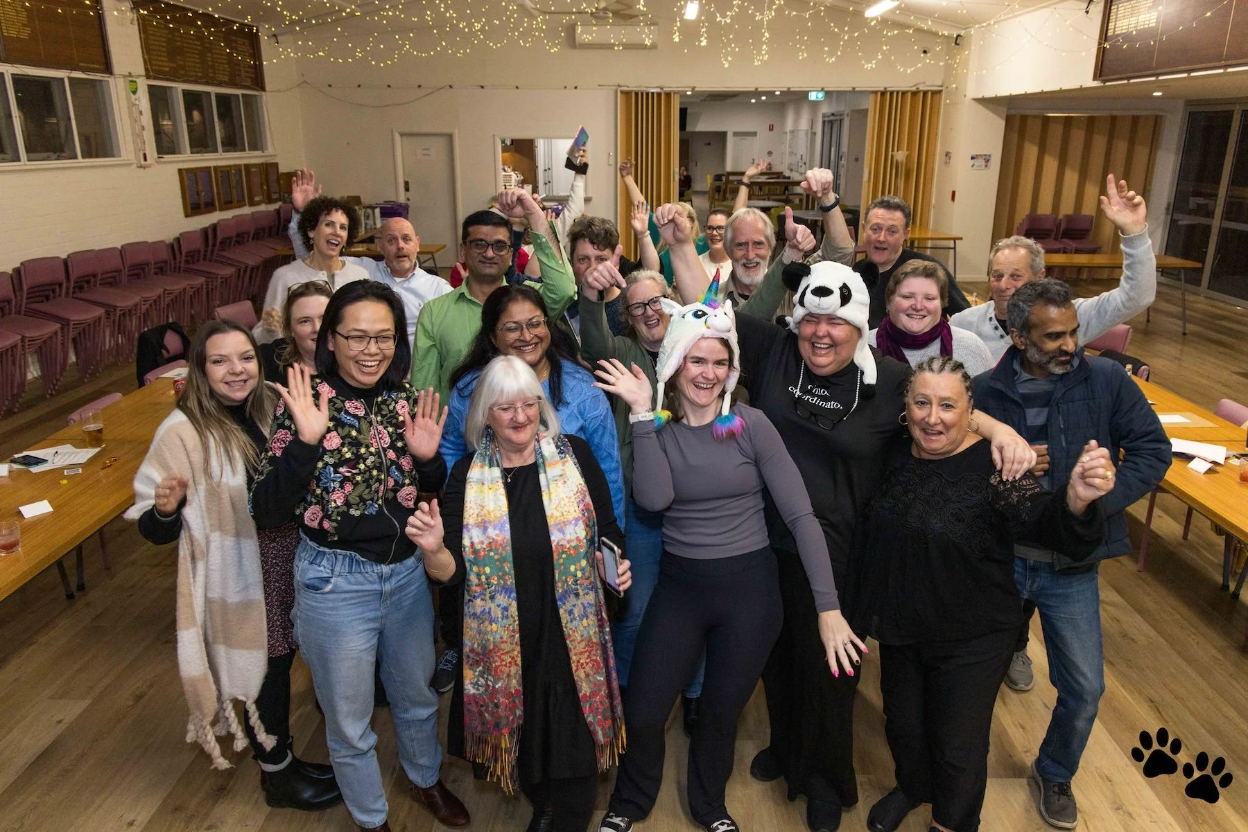 Group photo at a Bad Decisions Club event in a hall with fairy lights, people smiling and waving.