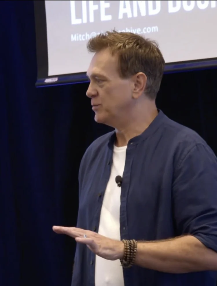 Close-up of Mitch Mitchem speaking on stage with one hand out