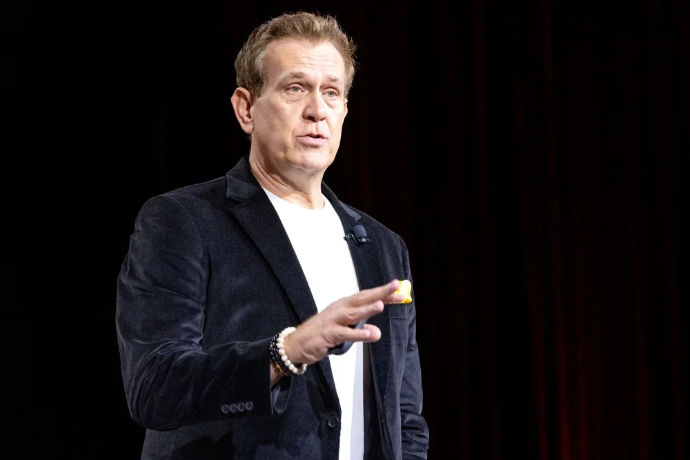 Mitch Mitchem speaking on stage against a black backdrop