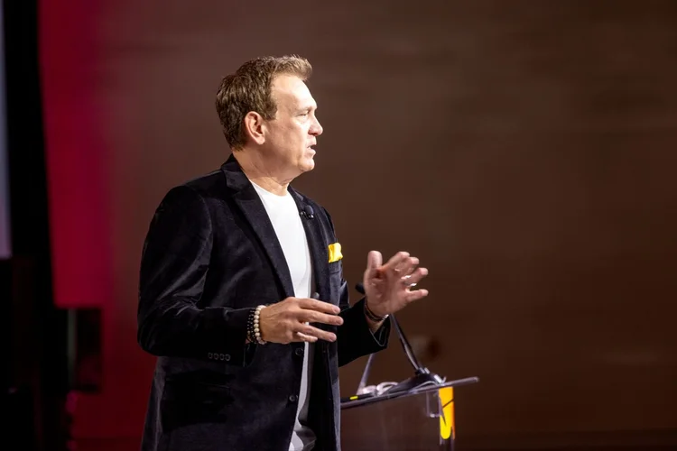 Mitch Mitchem speaking beside a podium on a red-lit stage