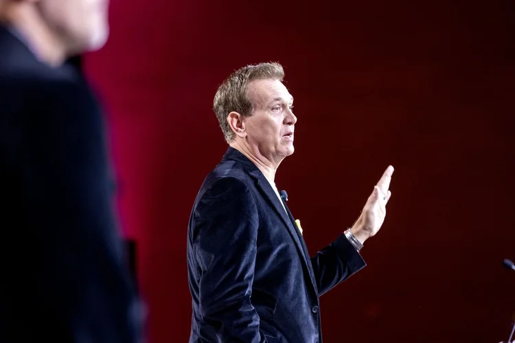 Mitch Mitchem raising one hand while speaking on a red-lit stage