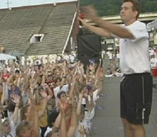 Outdoor crowd with arms raised, following a performer on stage