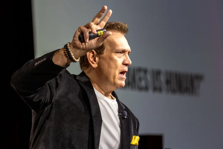 Mitch Mitchem with one hand raised mid-keynote in front of a projected slide