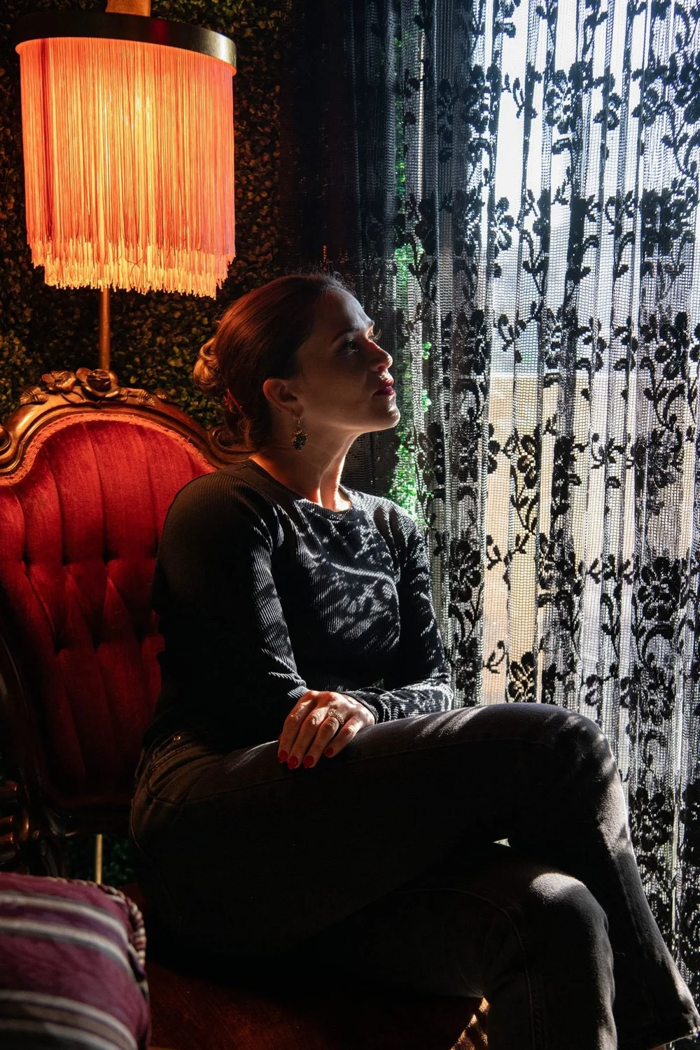 Liz in a red velvet chair by a lamp