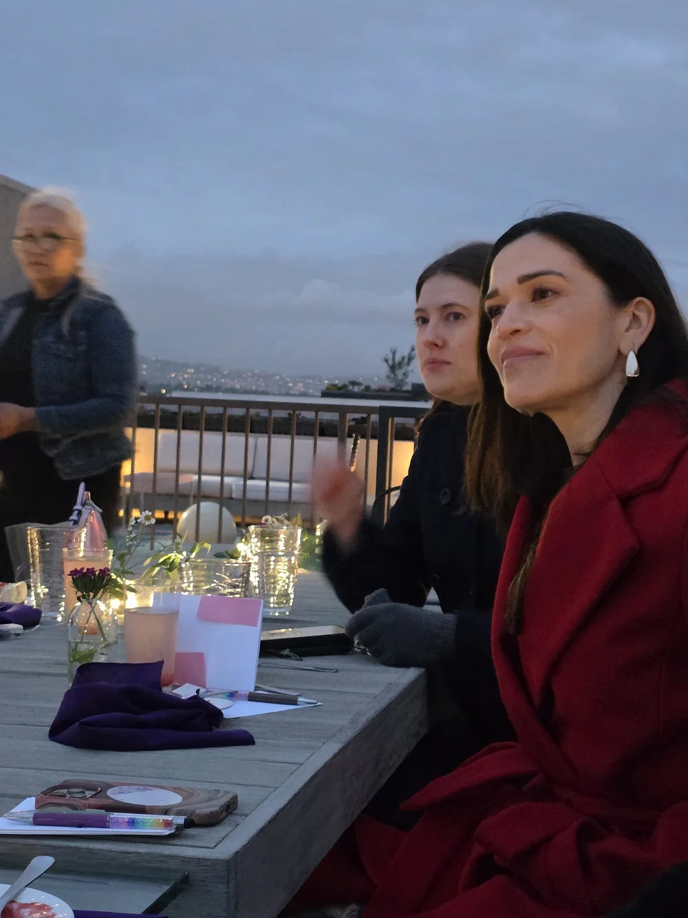 Women talking at a rooftop table at dusk