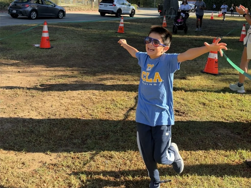 A young runner celebrates with arms wide open at the finish