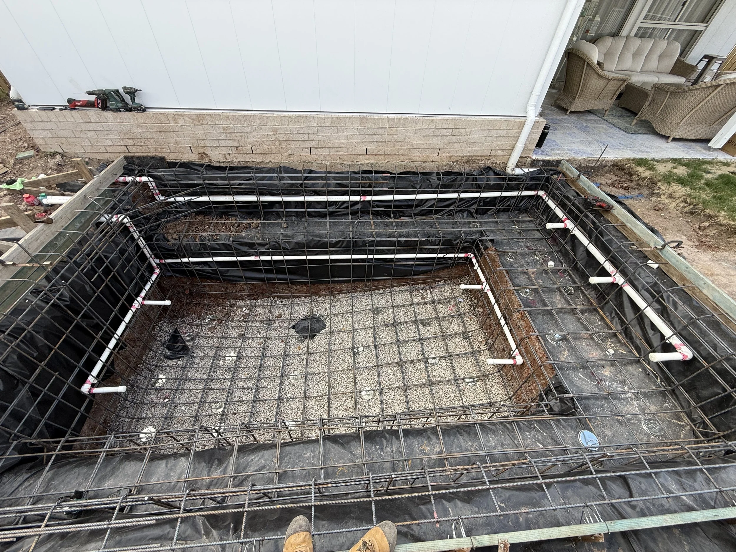 Steel reinforcement and pool plumbing lines run around a new concrete pool before shotcrete