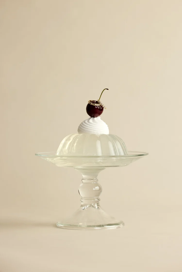 Gold diamond rings resting on a cherry atop a jelly on a glass cake stand