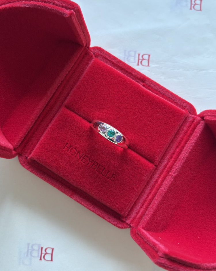 A gold ring set with three birthstones in a red HoneyBelle box