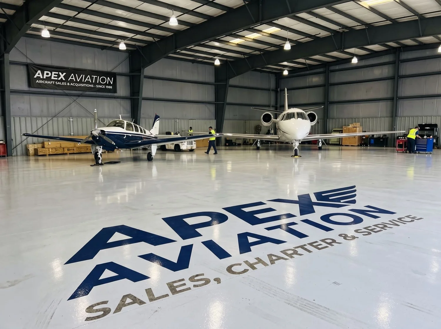 High-gloss light gray aircraft hangar floor with custom floor logo and aircraft