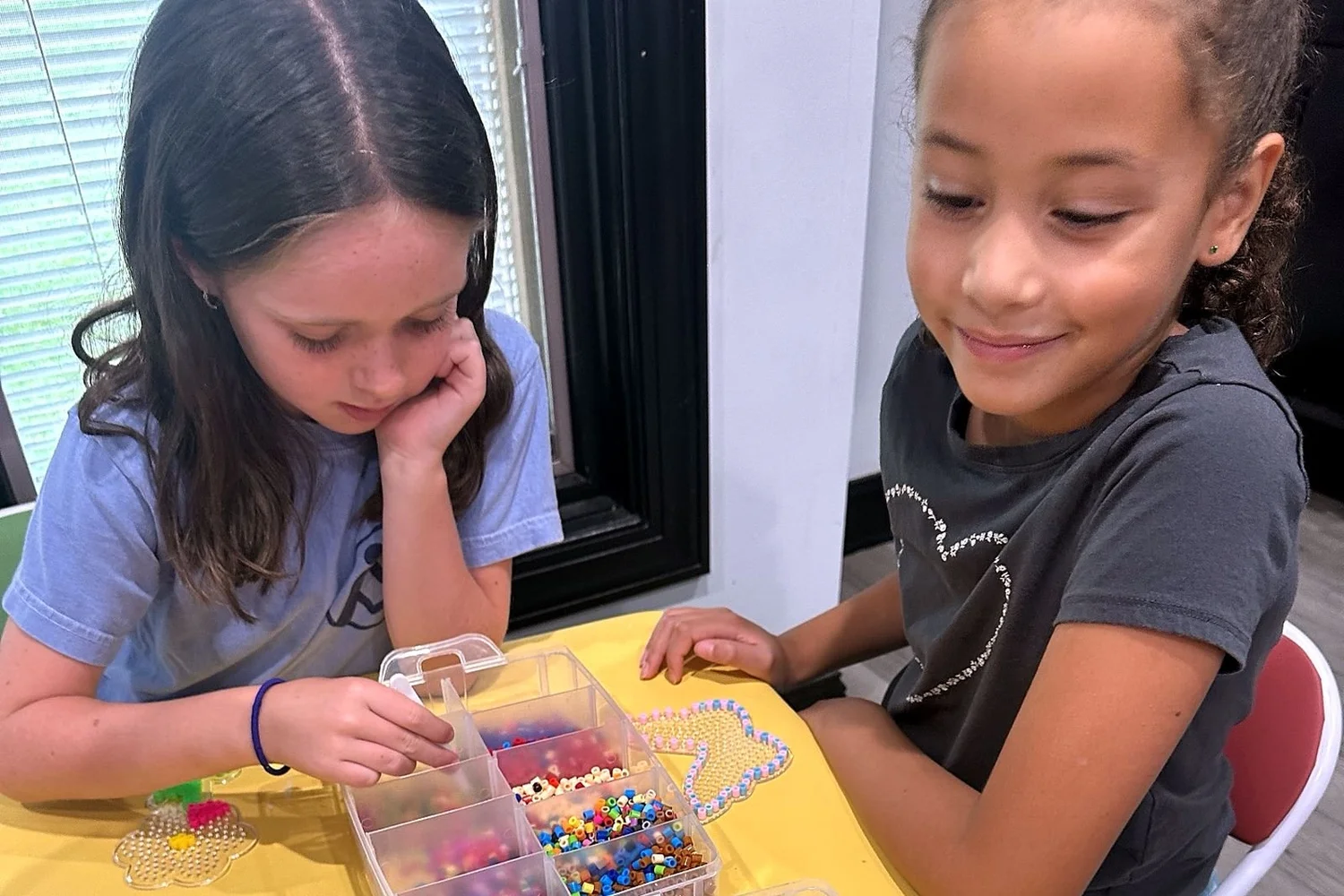 Two girls sharing a bead bin at a Clubhouse craft table