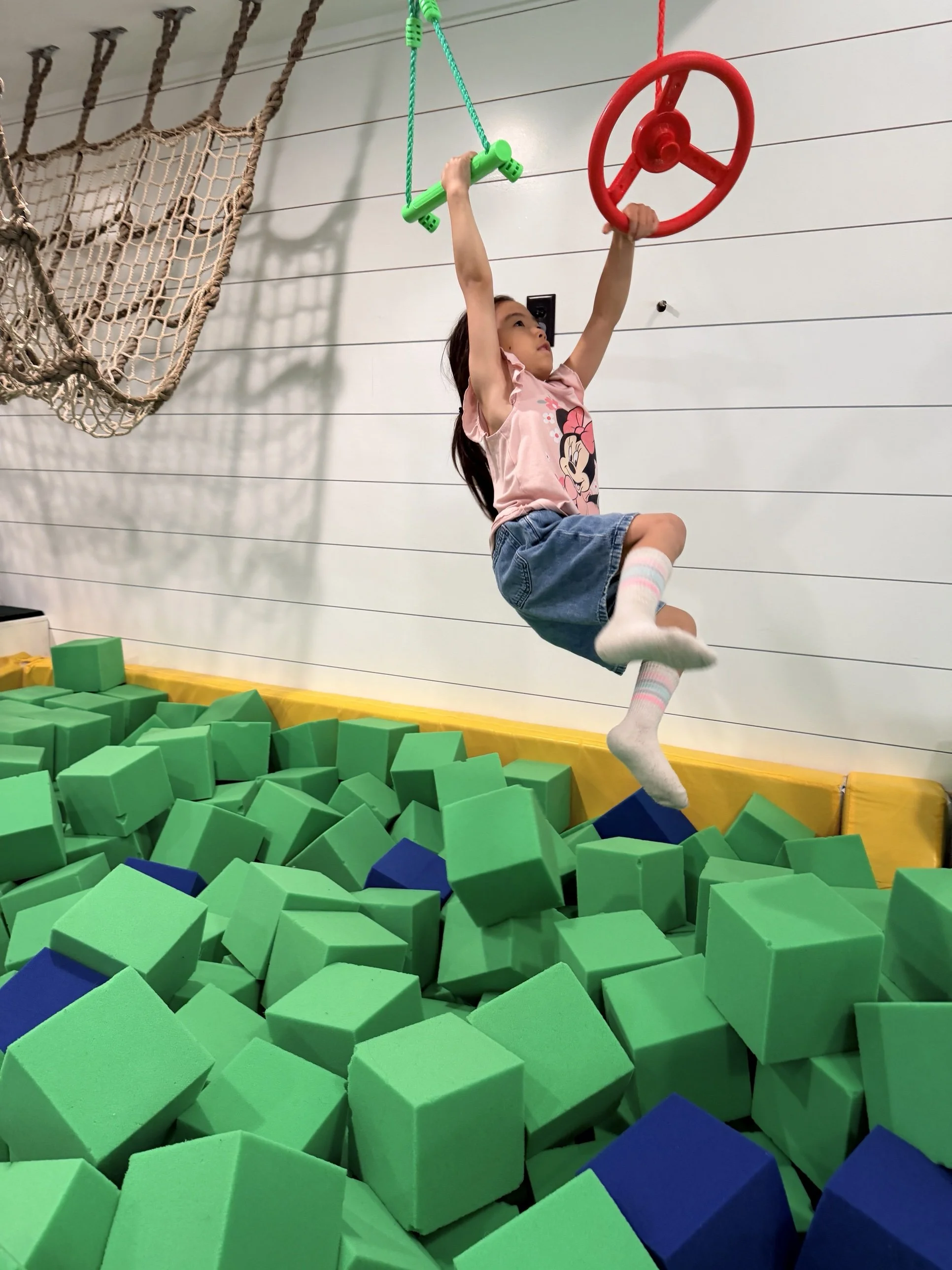 Child swinging from the trapeze over the foam pit