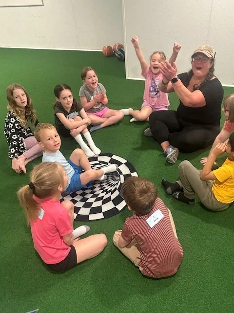 Instructor leading group circle time on indoor turf at The Clubhouse summer camp