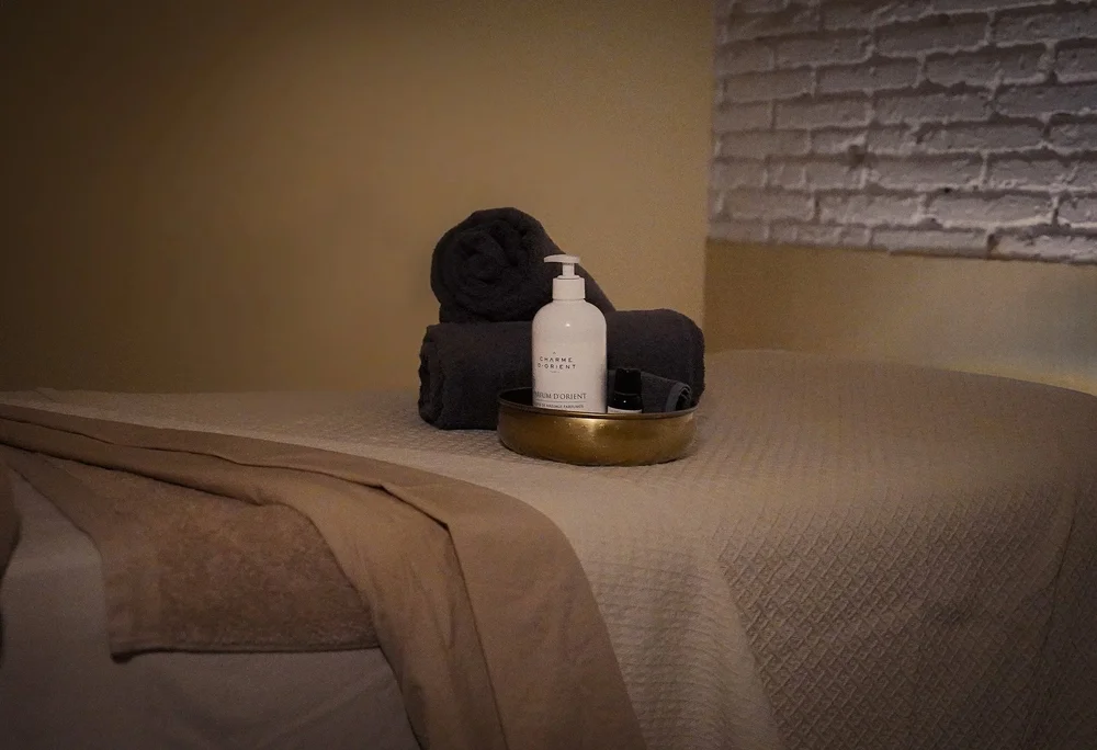 Rolled towels, massage oil and a brass bowl laid out on the treatment table