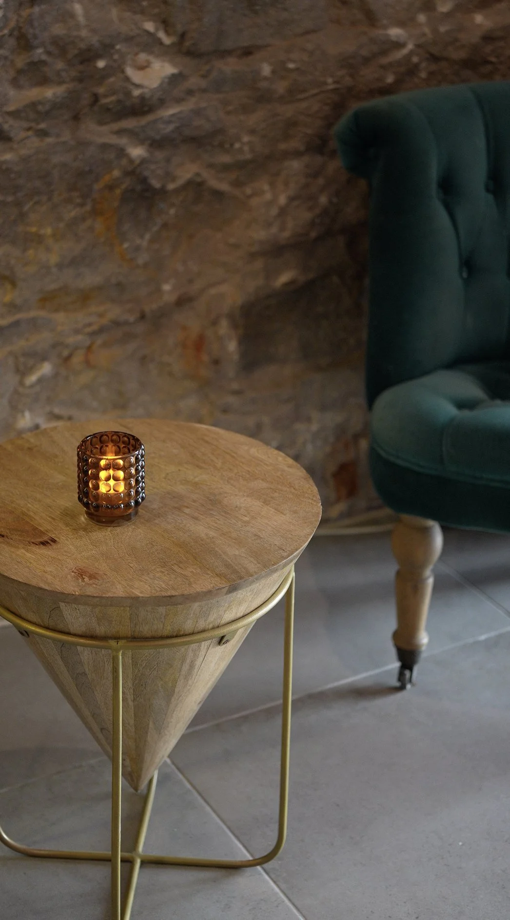 A candlelit side table and velvet armchair against the stone wall at the CHYL entrance