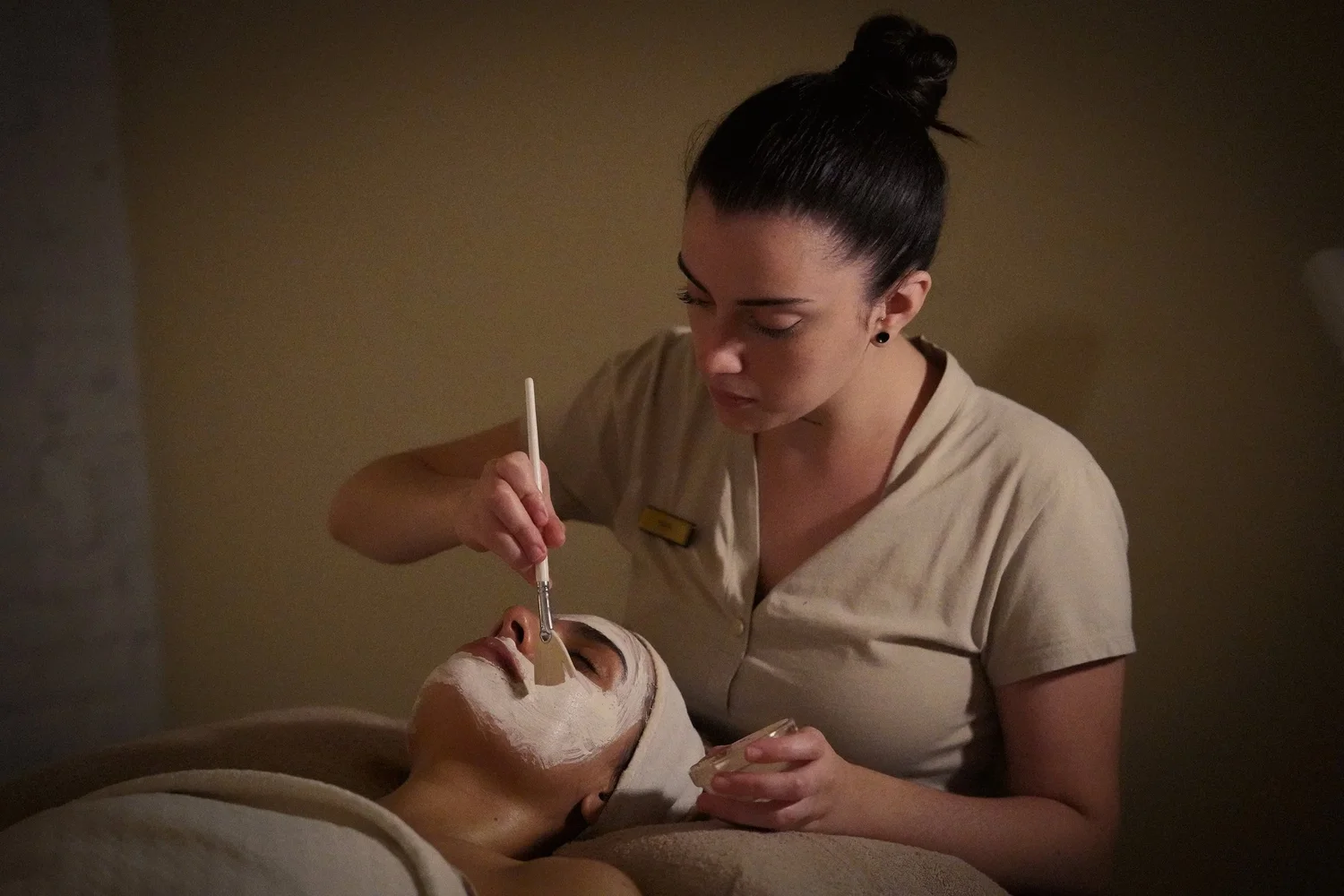 A therapist applying a facial mask with a brush