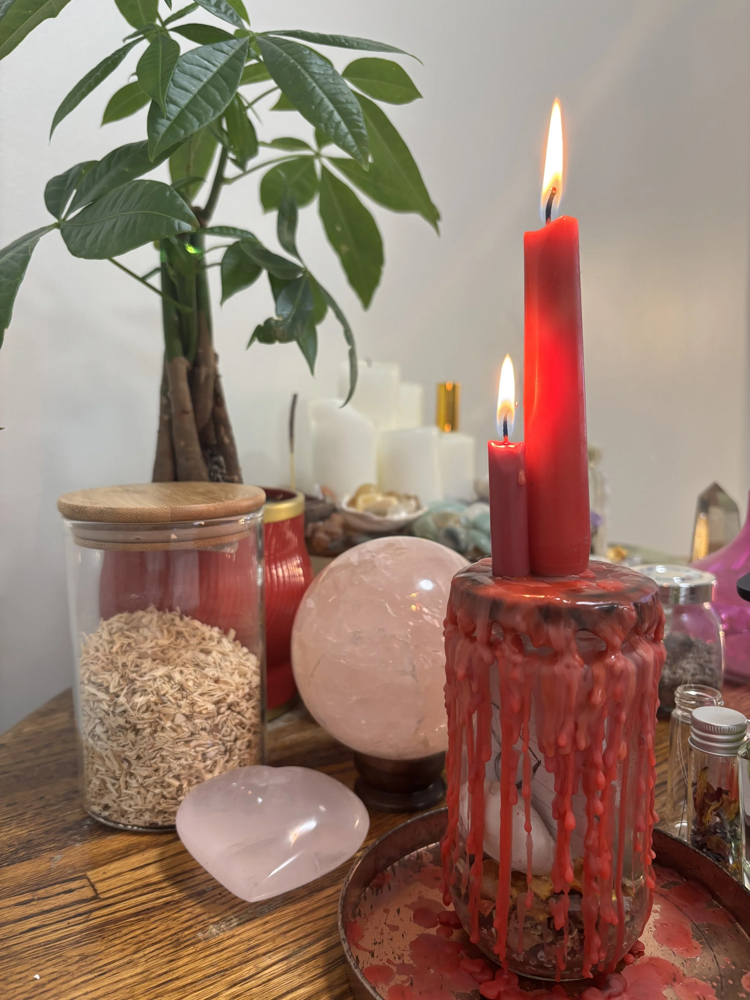 Red spell candles beside rose quartz and a green plant