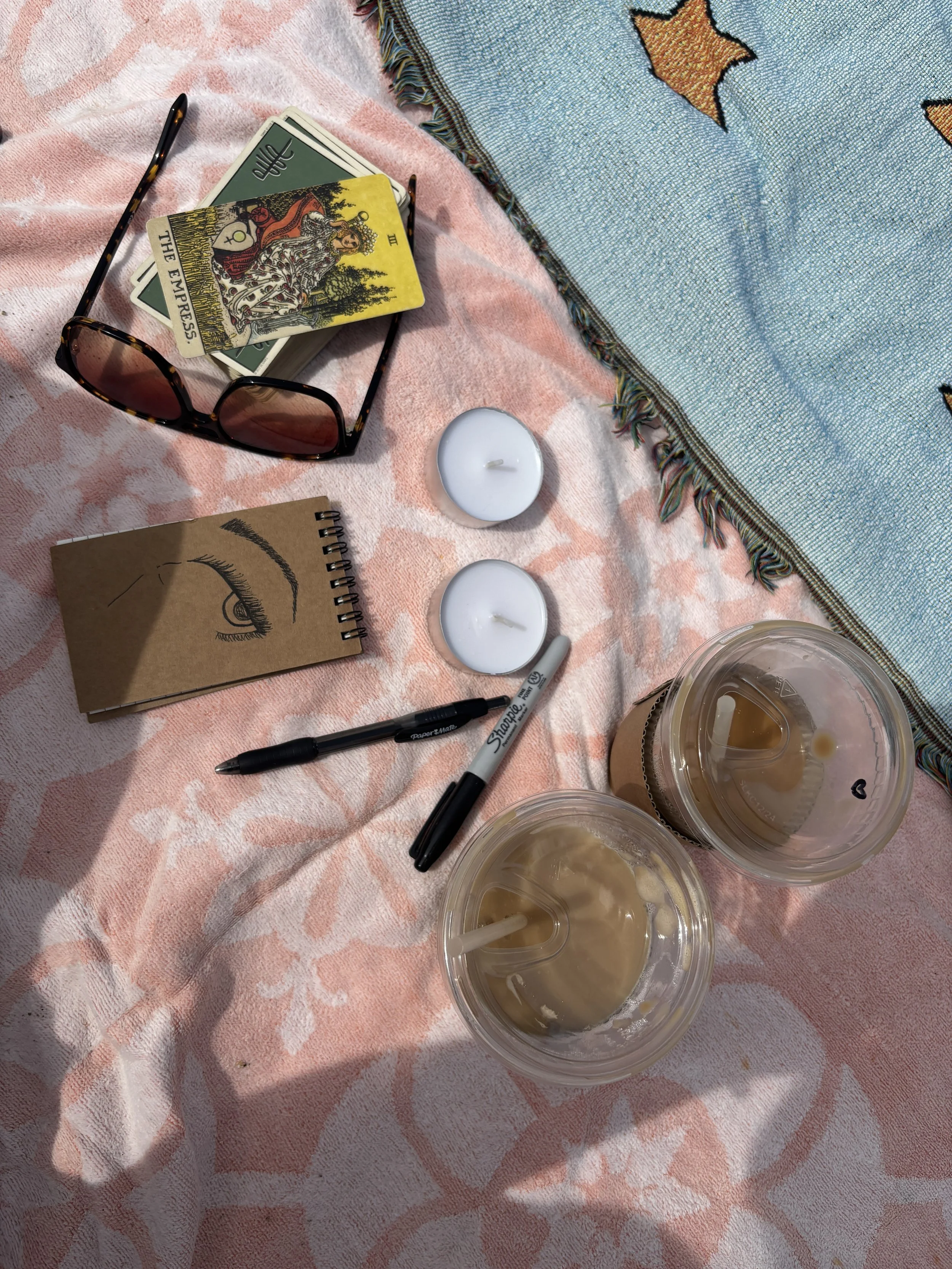 Tarot cards, a journal, candles and iced coffees on a pink picnic blanket