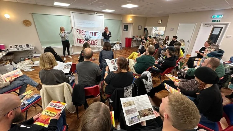 Two trainers holding a Free the MBR beagles banner in front of a seated group reading guides