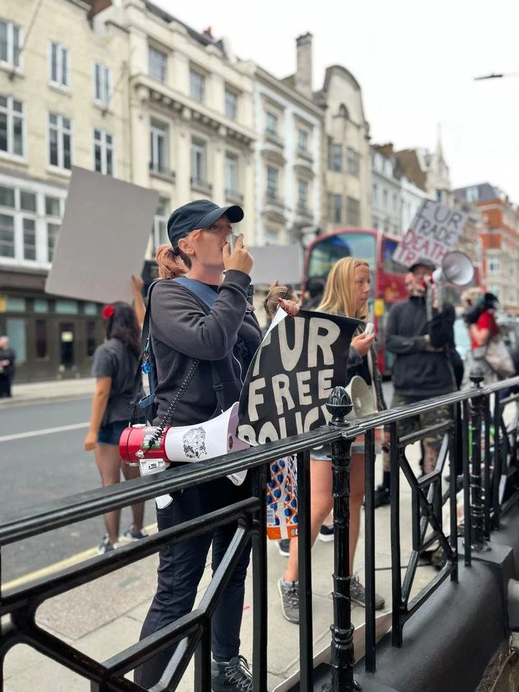 Activist speaking into a megaphone beside a Fur free policy placard on a city street