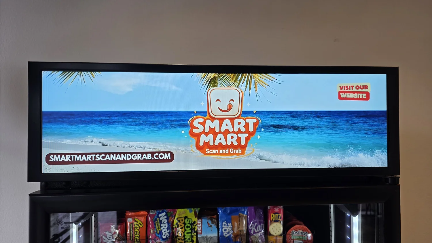 Close-up of a Smart Mart machine’s top display showing a beach video and custom branding