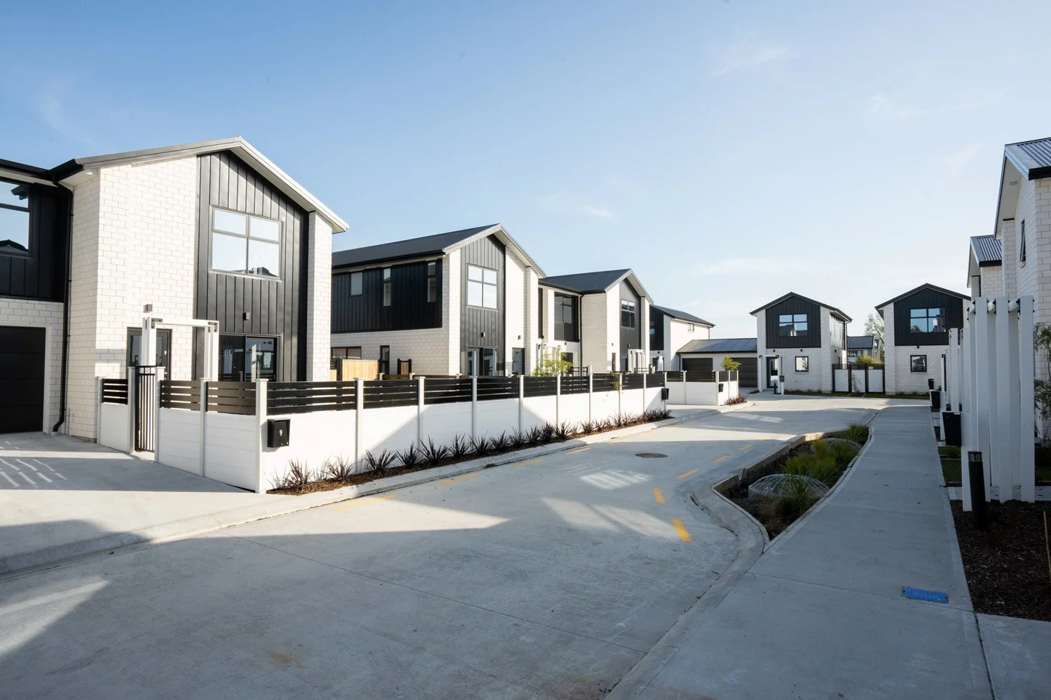 Completed homes at 10 Oliver Place, Upper Hutt, with white brick, dark gabled facades and a shared landscaped lane