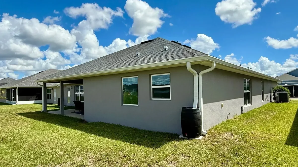 White seamless gutters and downspout connected to a rain barrel on a home in Citrus Springs, Florida.