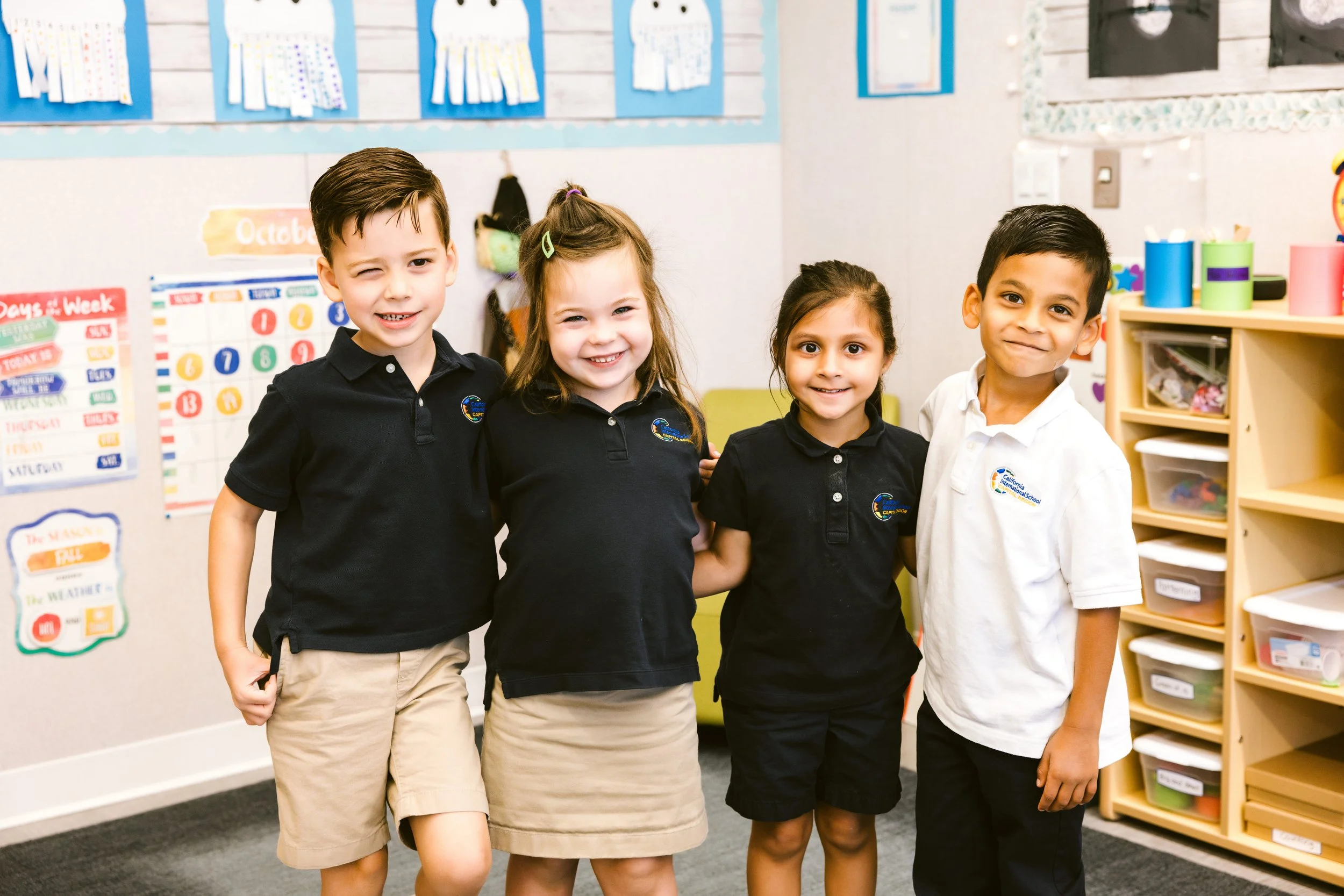 Four elementary students in school uniforms smiling together in bright classroom