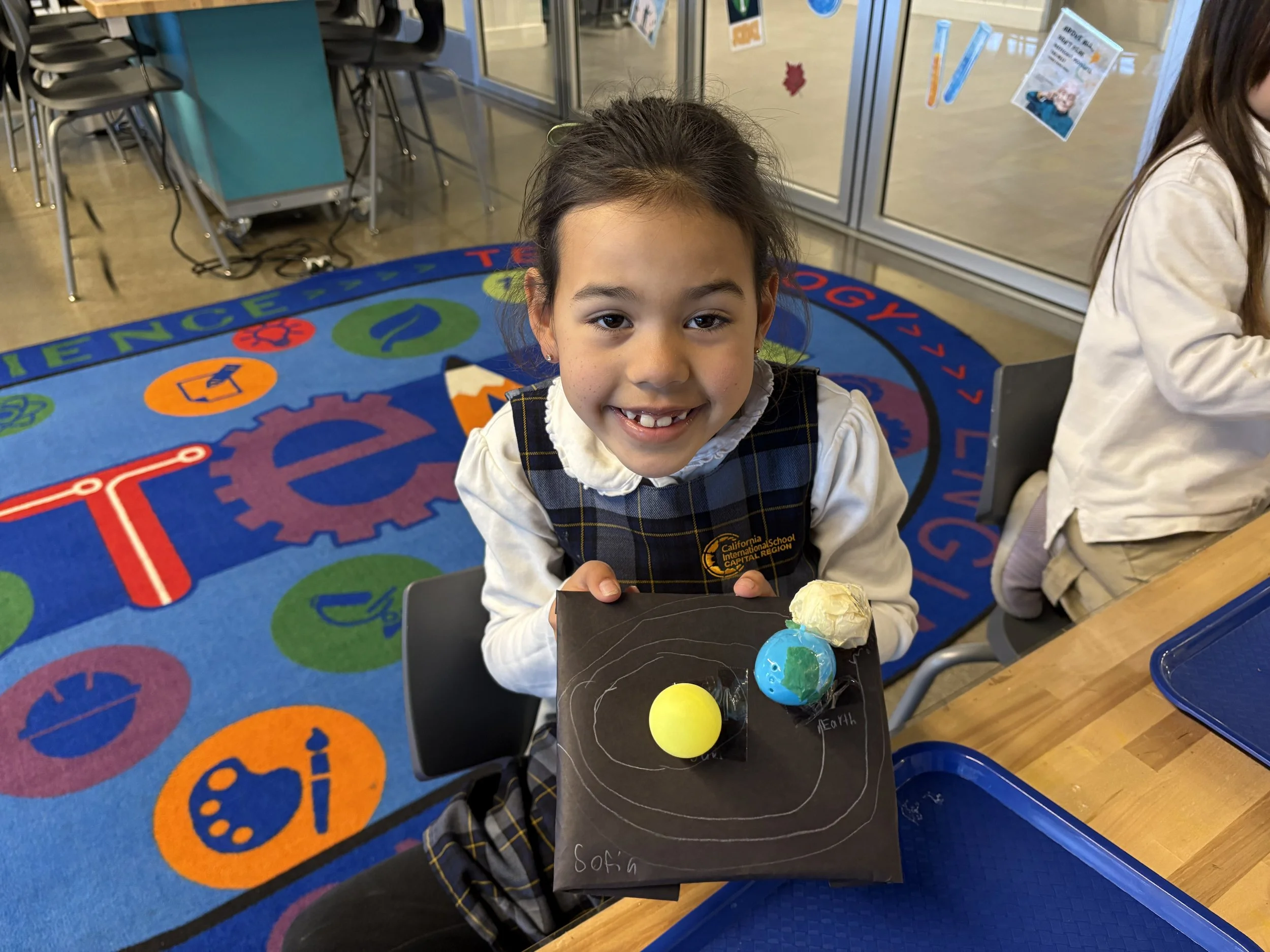 Young girl confidently presenting her creative artwork to the camera, reflecting CIS's student-centered academic approach