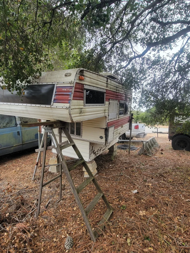 Older truck camper on supports under trees