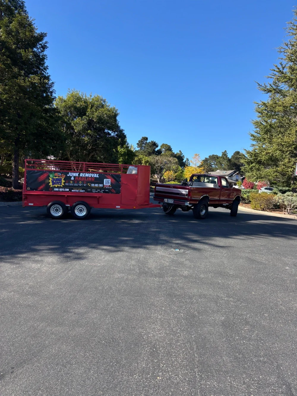 Junk Boys red pickup truck and branded junk removal trailer on a tree-lined street