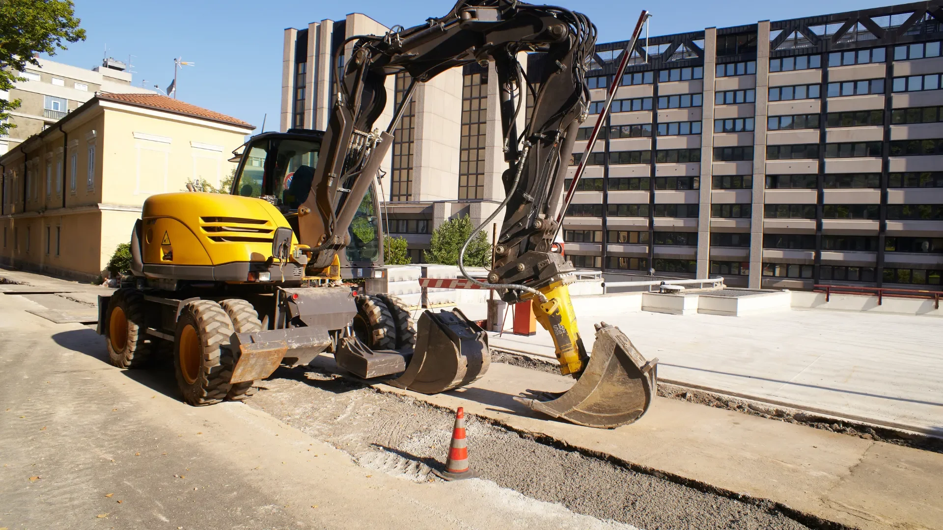 Yellow excavator digging a deep pit through stone and soil
