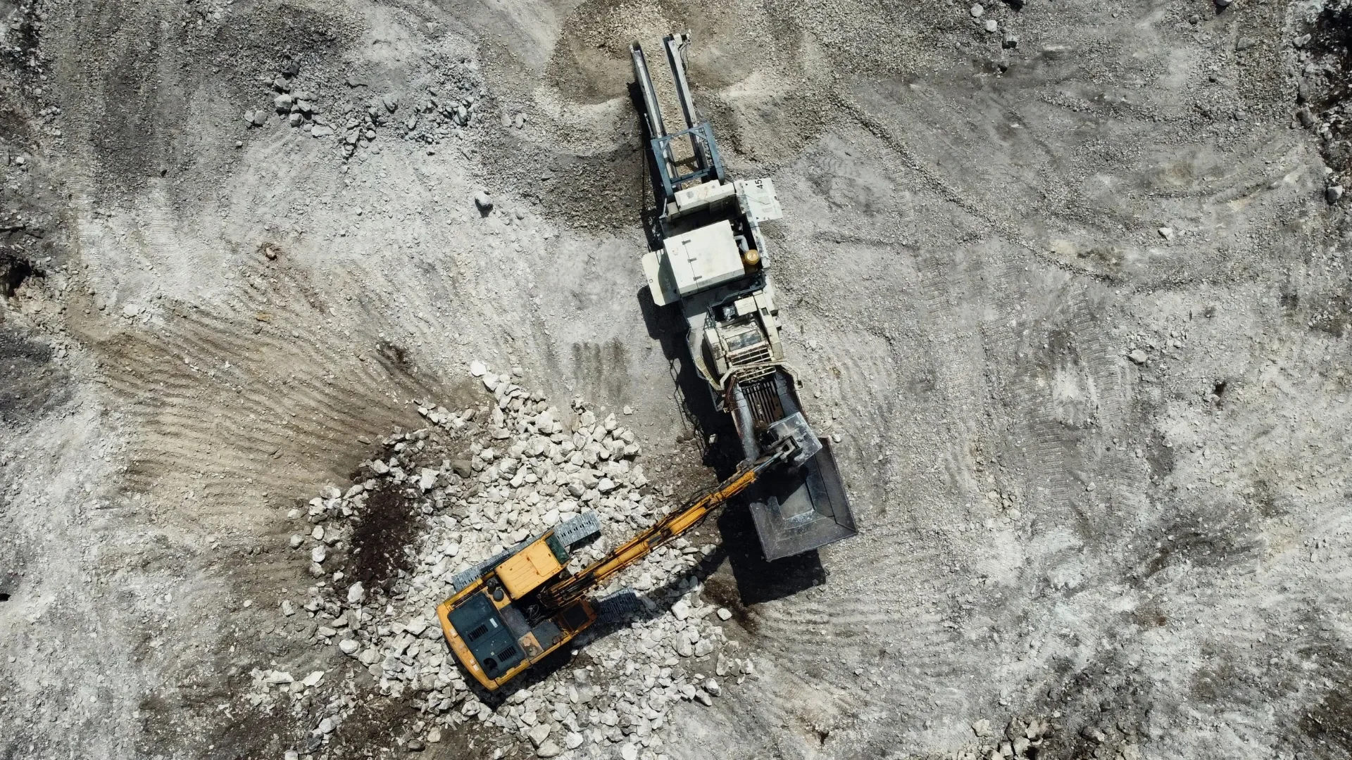 Excavator feeding broken concrete into a mobile crusher for removal and recycling