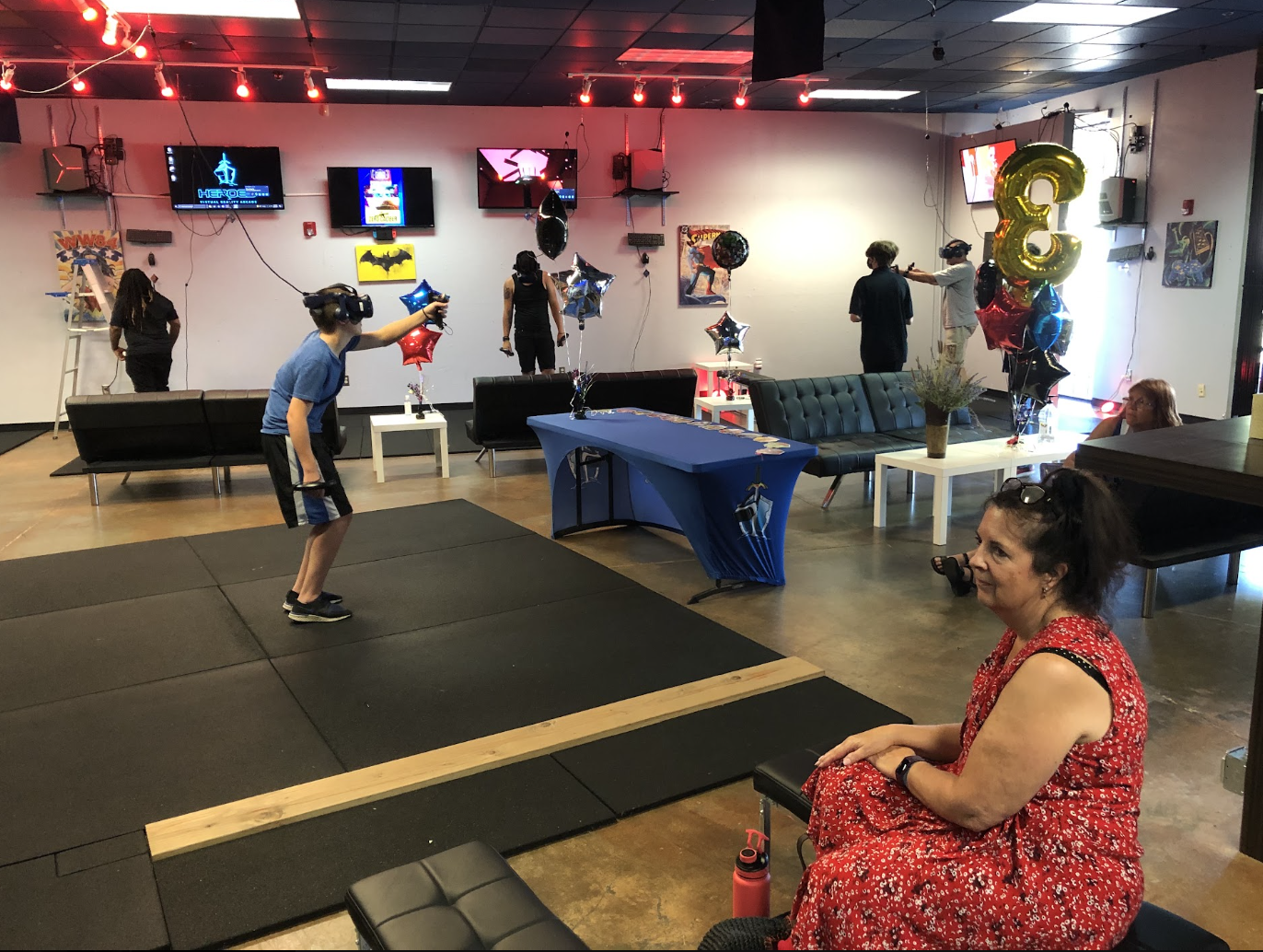 Birthday party guests using VR headsets and controllers while others watch from lounge seating.
