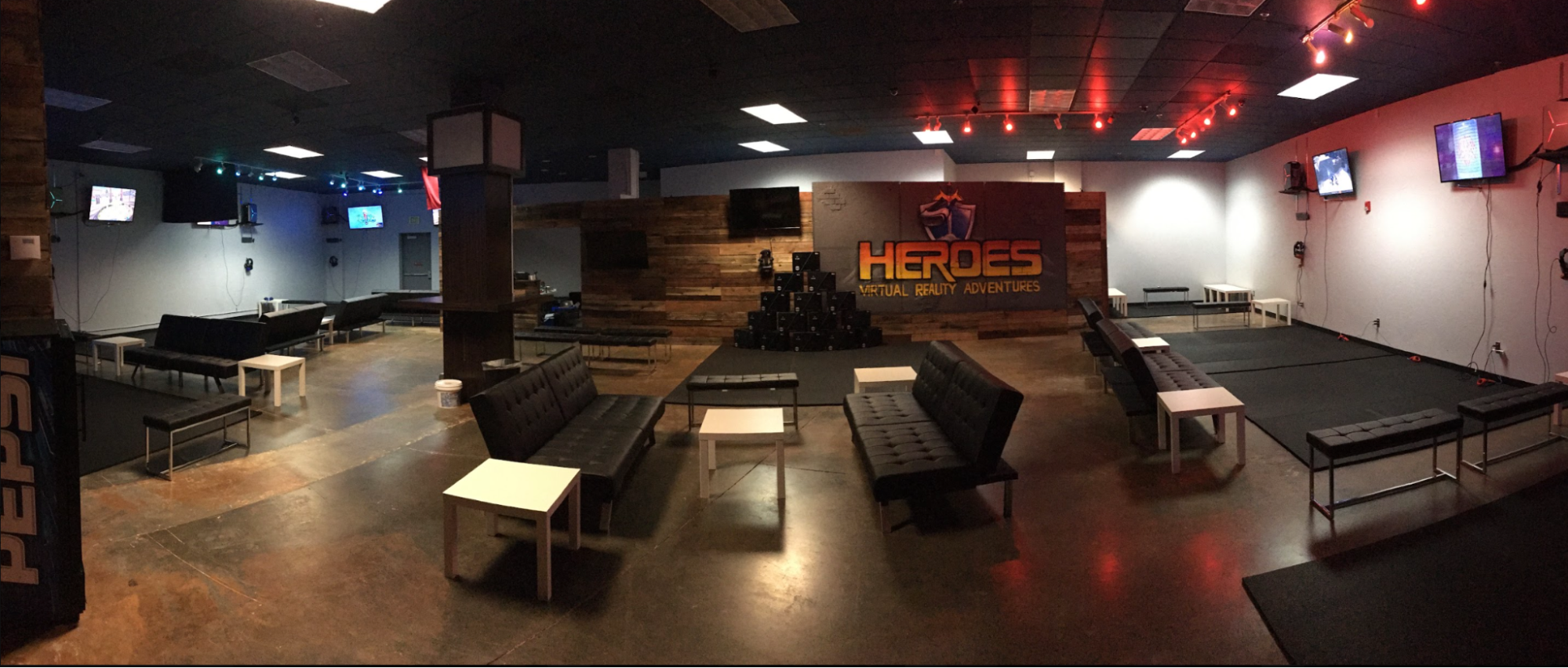Panoramic view of HEROES VR Adventures with padded play areas, wall-mounted screens, and lounge seating.
