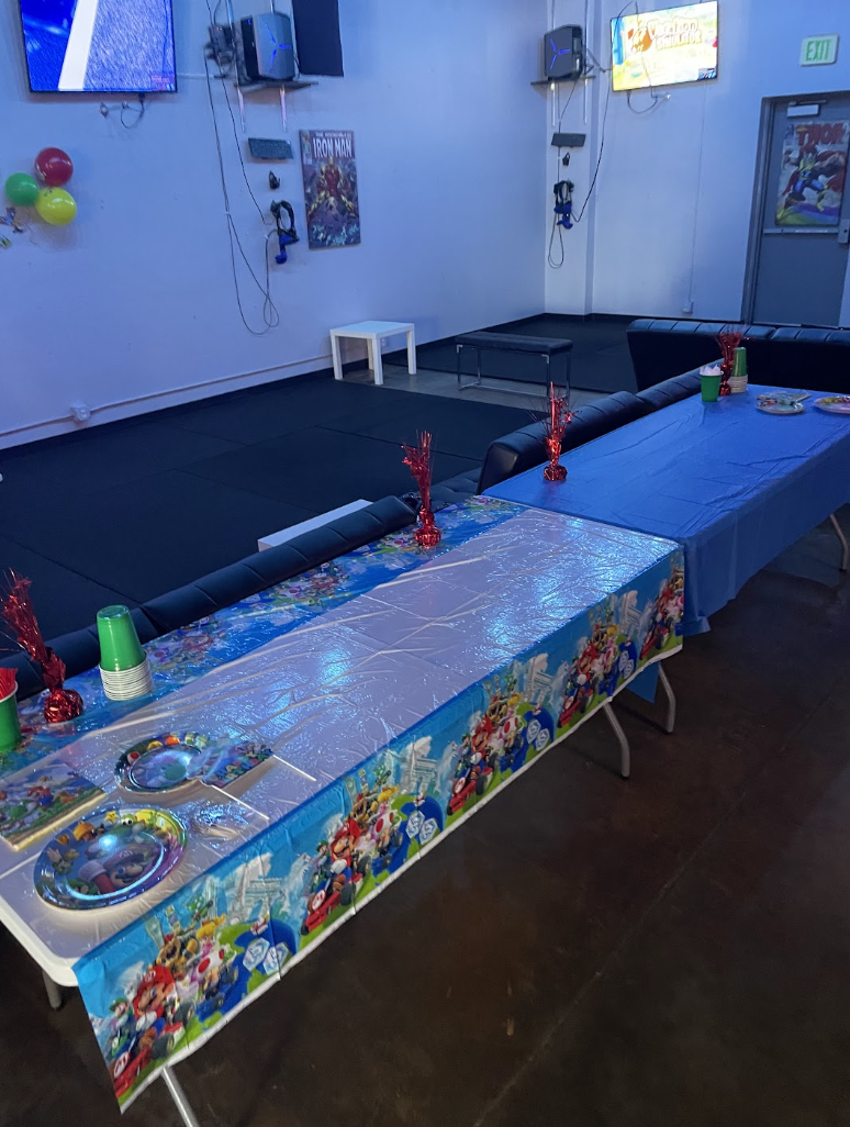 Birthday party tables with Super Mario decorations, plates, and cups beside VR play areas.