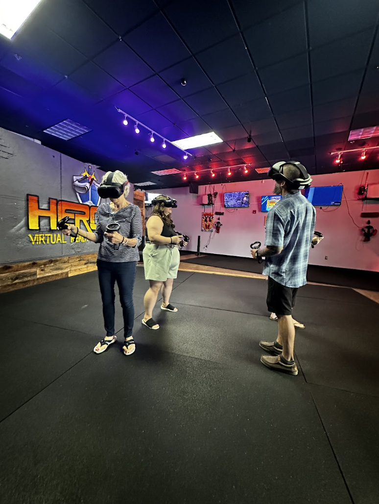 Adults using VR headsets and motion controllers in the play area at HEROES VR Adventures.