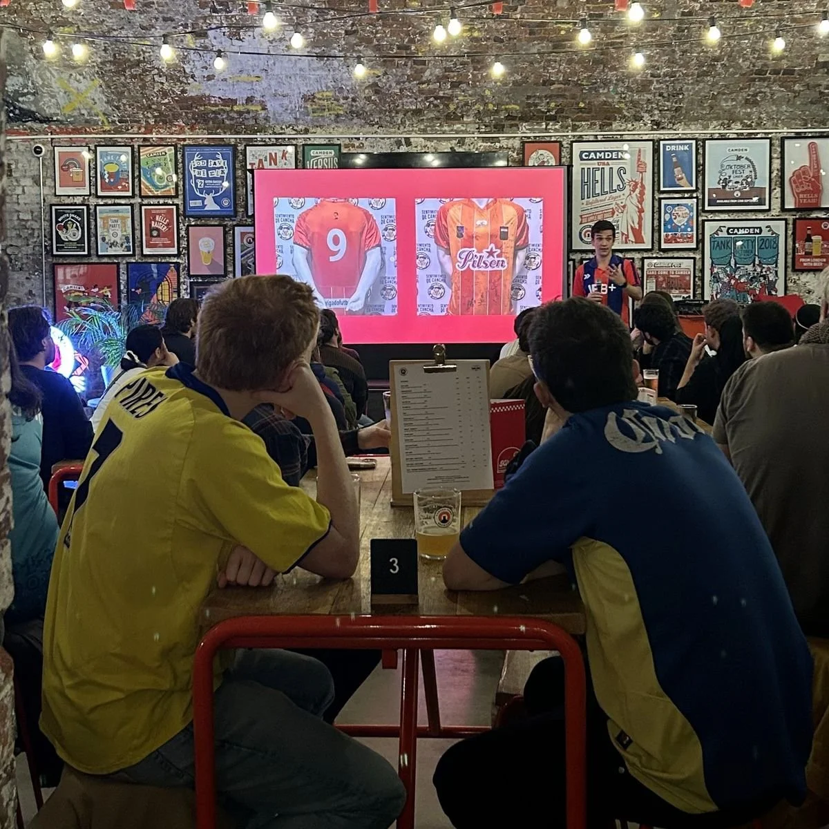 Audience in football shirts watching a talk at a Camden brewery