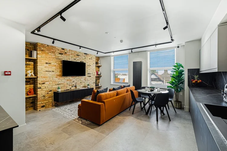 The same space finished: open-plan living and kitchen with exposed brick and track lighting