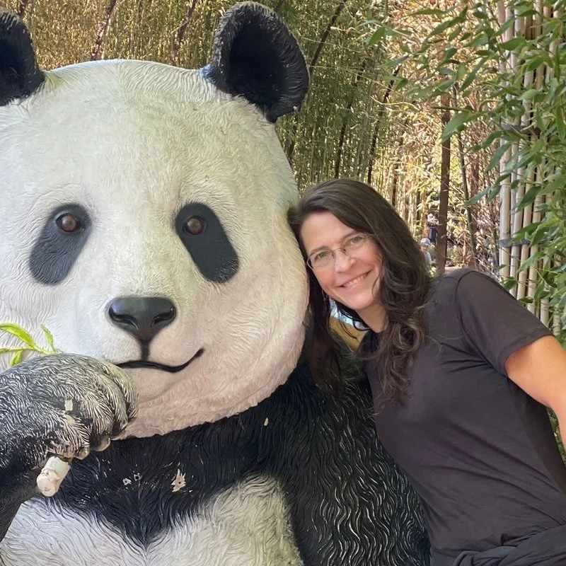 Becca Darr leaning against a giant panda statue in a bamboo grove.